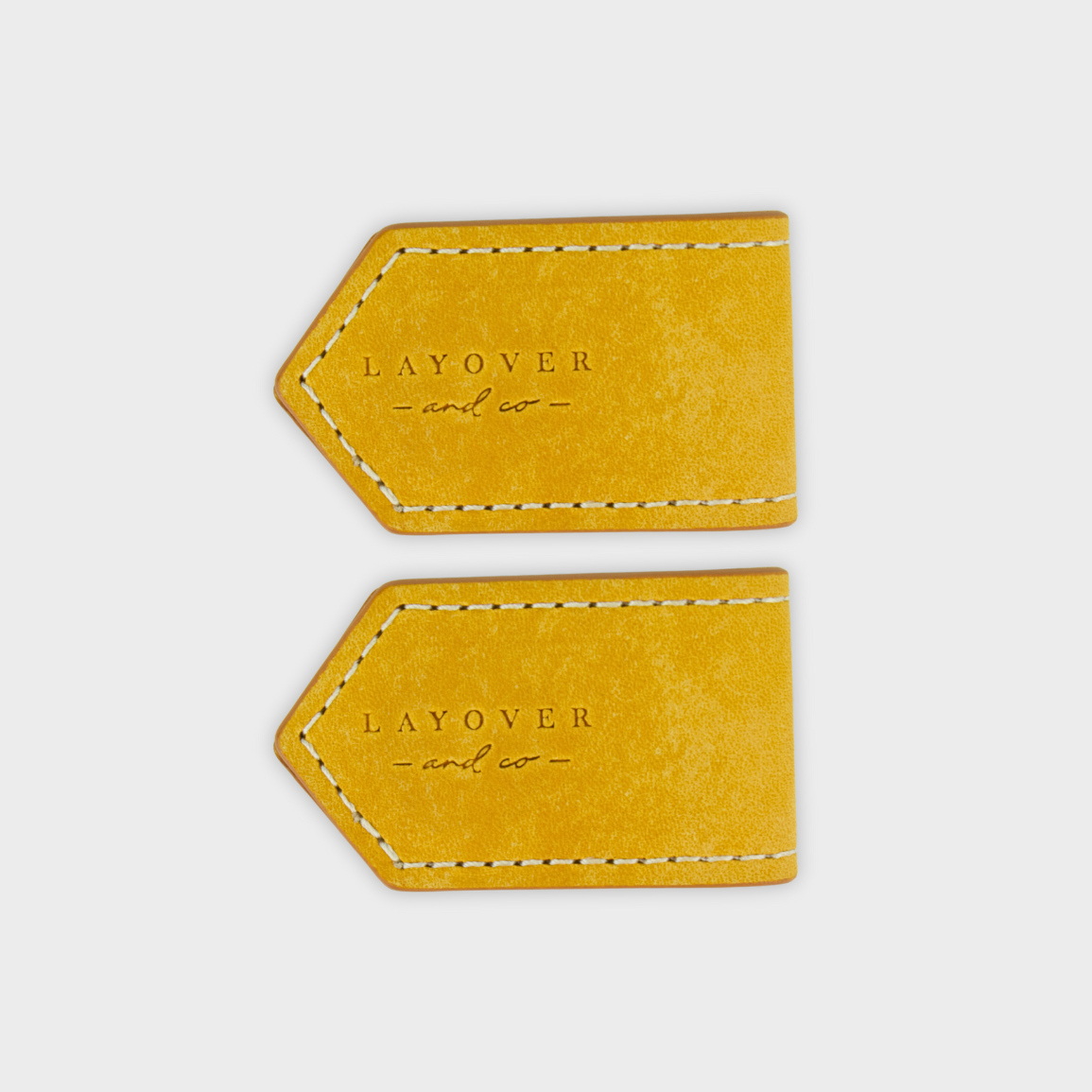 Two mustard yellow leather bookmarks with 'LAYOVER' and 'co.' text on a light gray background.