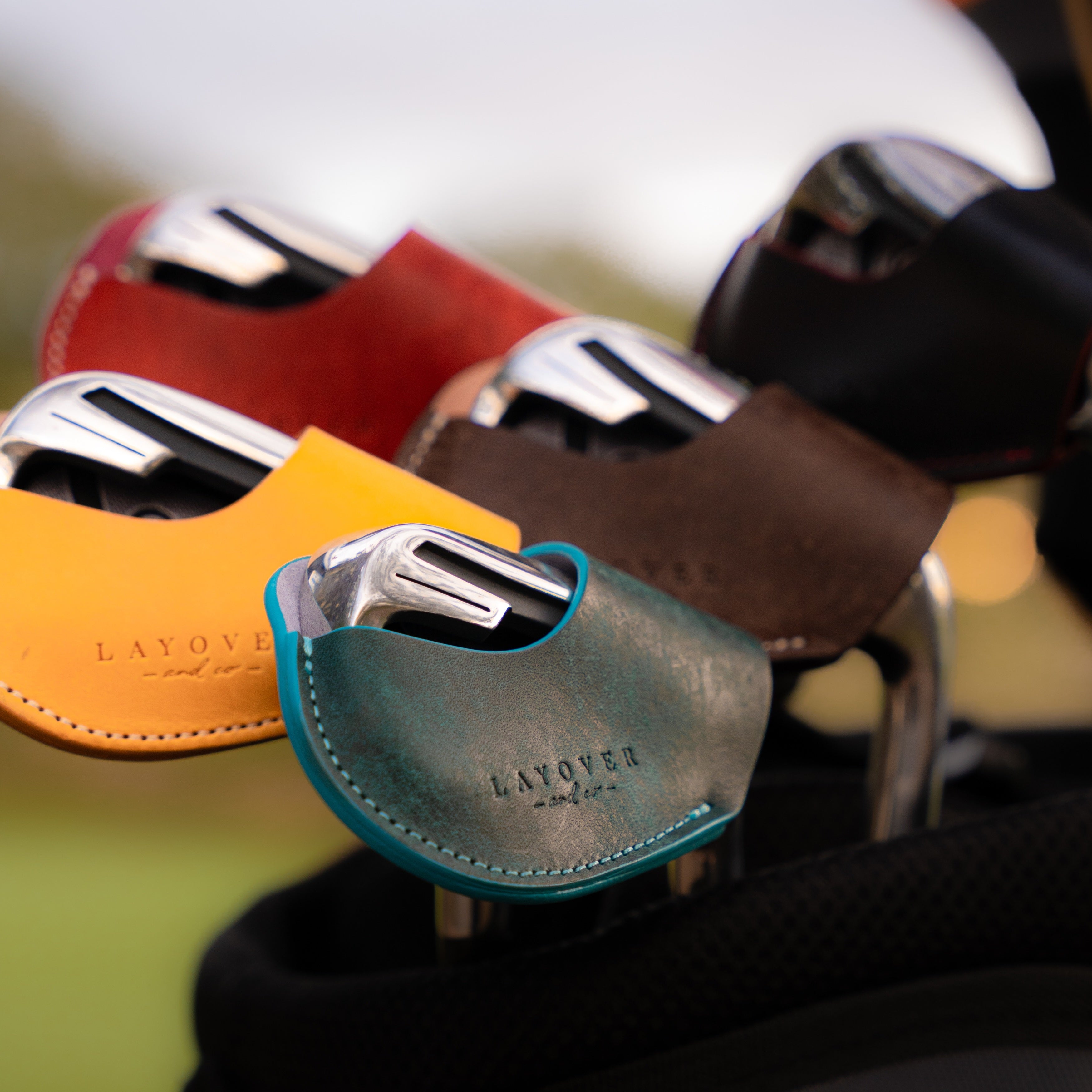 Five leather golf iron covers in black, dark brown, yellow, green and red, showcasing smooth vegetable-tanned leather and precise stitching.