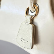 Close-up of a cream-colored leather hat holder from Layover and Co., elegantly attached to a matching leather handbag with gold hardware. The premium textured leather and fine craftsmanship highlight the stylish and functional design, perfect for travelers and fashion enthusiasts.