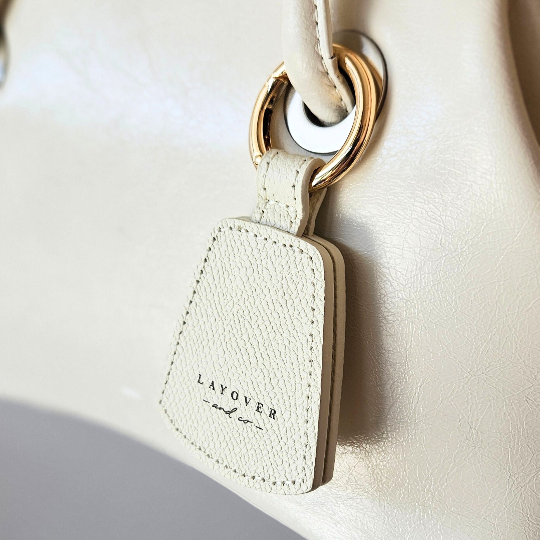 Close-up of a cream-colored leather hat holder from Layover and Co., elegantly attached to a matching leather handbag with gold hardware. The premium textured leather and fine craftsmanship highlight the stylish and functional design, perfect for travelers and fashion enthusiasts.