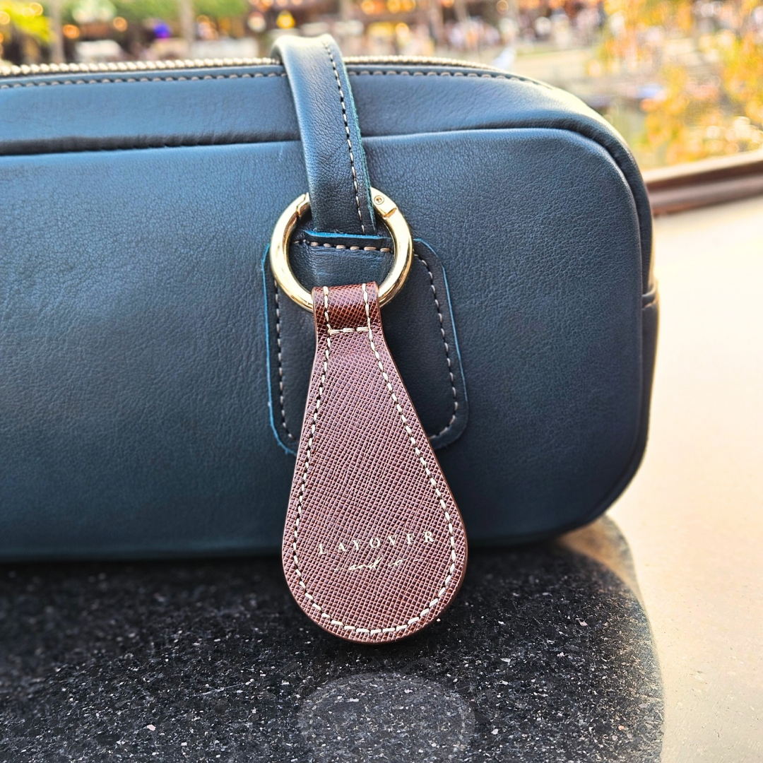 Close-up of Layover’s leather magnetic hat holder in brown, attached to a dark teal leather bag with gold hardware. The holder features textured leather and precise stitching, showcasing premium craftsmanship.